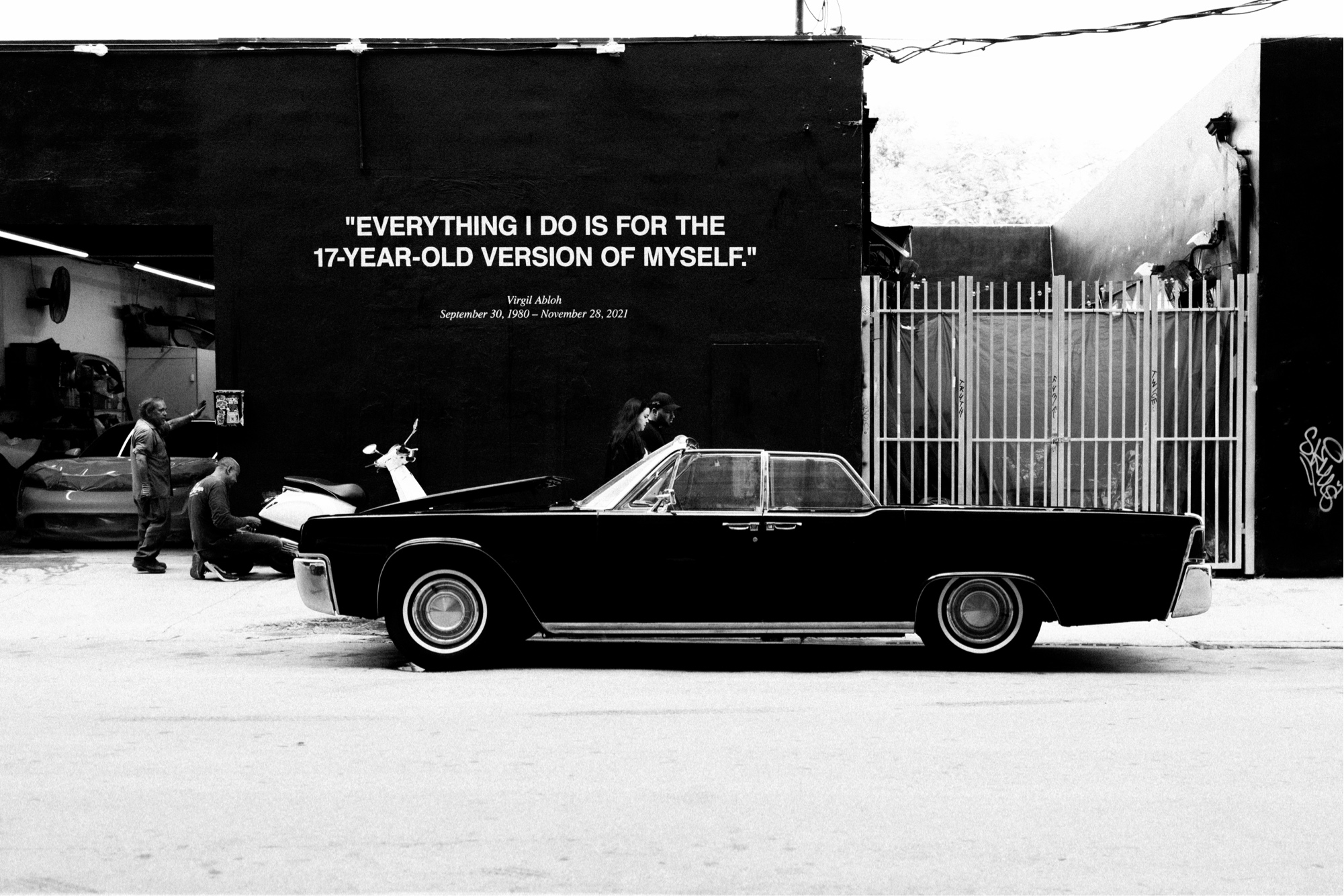 Black-and-white street photograph from Miami — a 1960s convertible parked outside a building with a hand-painted memorial quote, 'Everything I do is for the 17-year-old version of myself.'